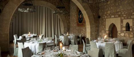 A restaurant with round tables set for dining, featuring candlelight and stone walls.