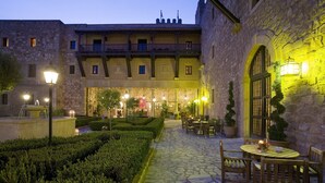 Une cour dallée de pierres, avec une fontaine et un espace repas comprenant des tables et des chaises.