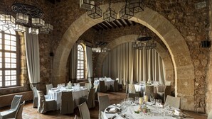 Un restaurant avec des tables rondes disposées pour le service, des murs en pierre et des lampes suspendues de style lanterne.