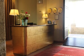 Un mostrador de recepción con dos lámparas, un florero con flores y un certificado enmarcado en la pared.