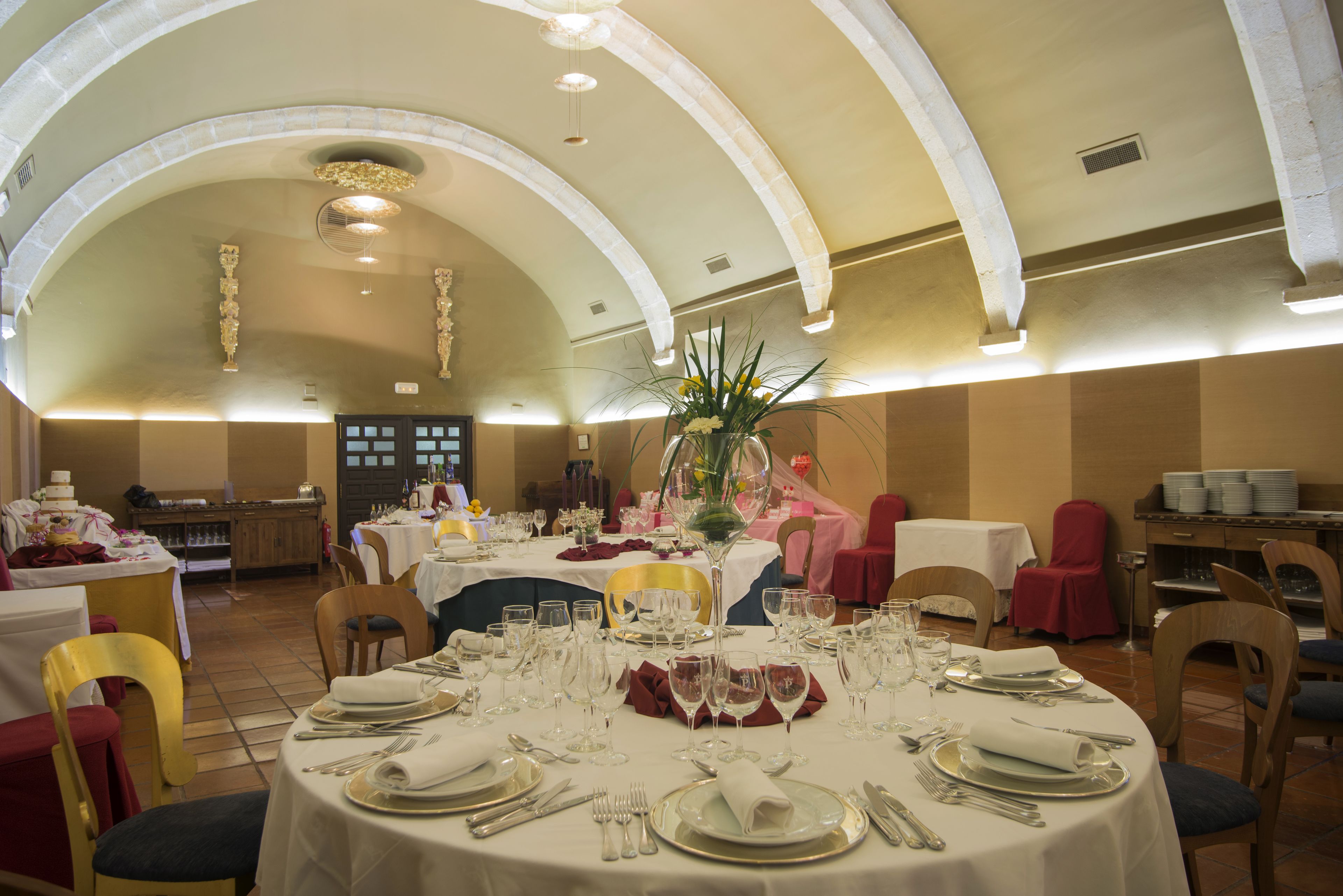 Un salón de banquetes con mesas redondas dispuestas para comer, con manteles blancos, cubertería y cristalería.