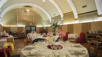 Un salón de banquetes con mesas redondas dispuestas para comer, con manteles blancos, cubertería y cristalería.
