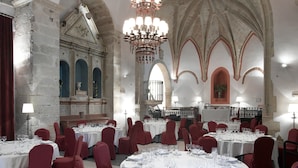 Un salón de banquetes con mesas redondas, sillas rojas y un techo alto abovedado.