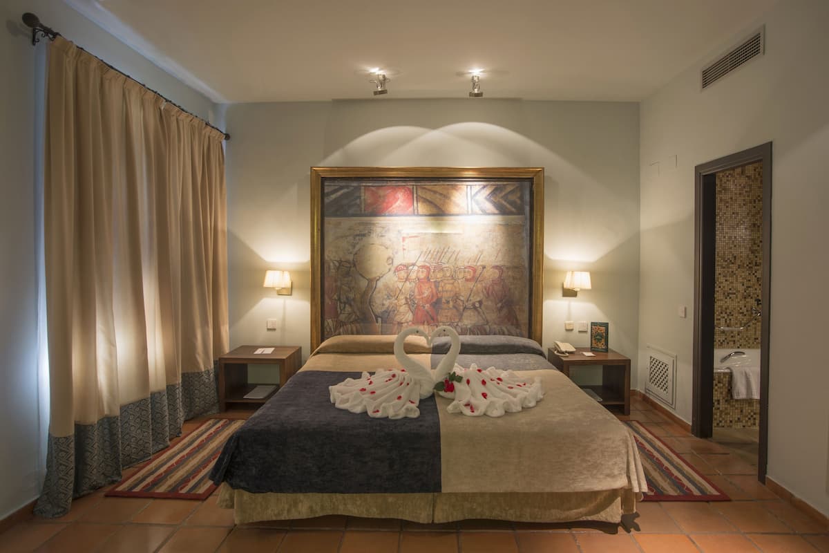 Ein Hotelzimmer mit einem großen Bett, zwei Nachttischlampen, einem Wanddekor und einem durch eine offene Tür einsehbaren Badezimmer.