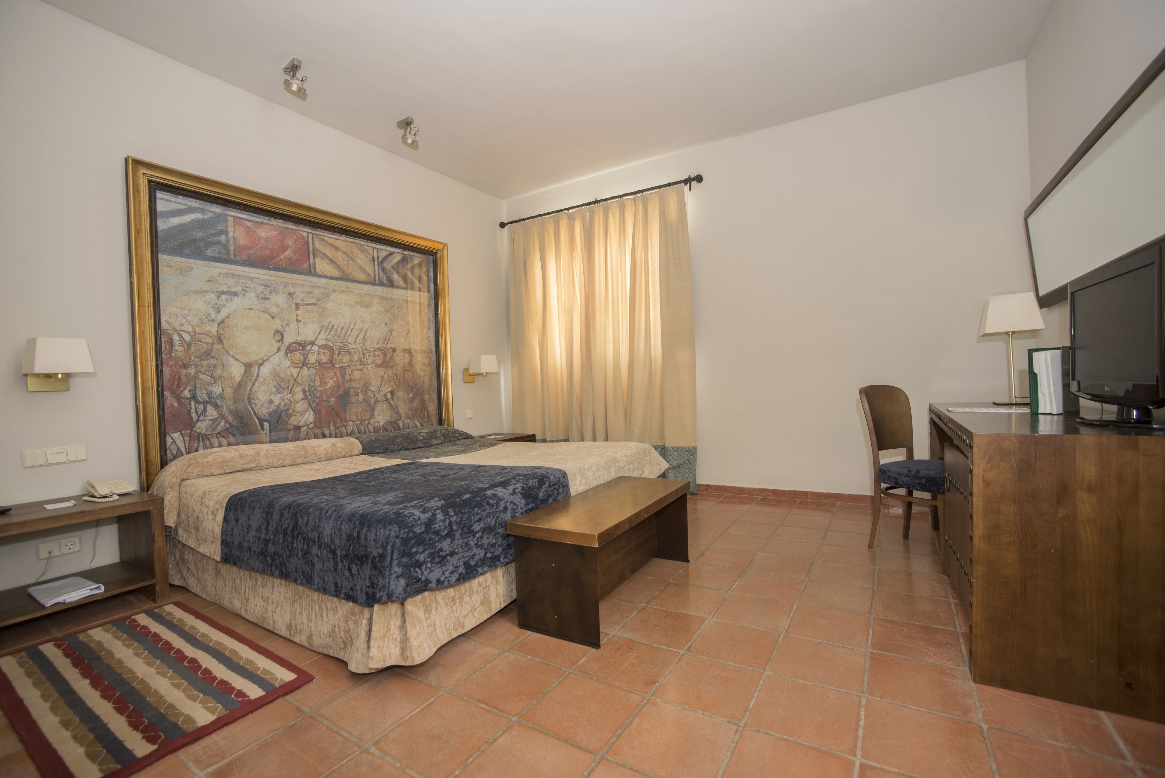 Hotelkamer met een bed, een bureau, een stoel, een televisie en een schilderij aan de muur.