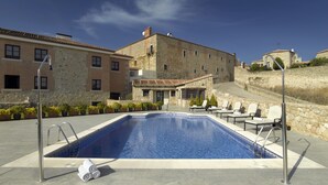 Una piscina con sillones de descanso y un edificio de piedra al fondo.