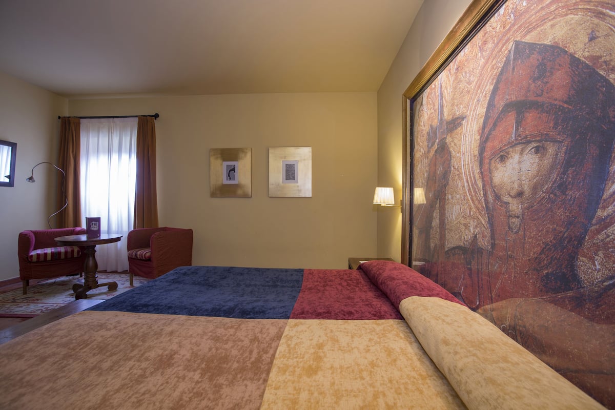 Ein Hotelzimmer mit einem großen Bett, einem Schreibtisch, zwei Stühlen, einer Lampe und einem Bild an der Wand.