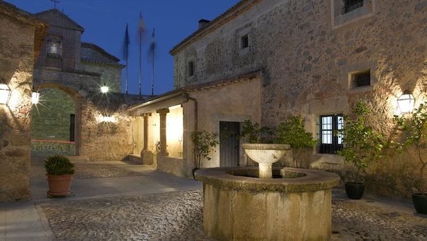 Un patio histórico de piedra con suelo adoquinado, una fuente central y edificios de arquitectura tradicional.