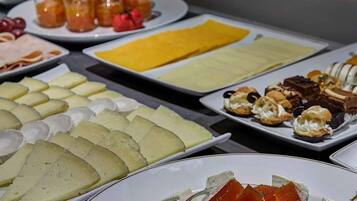 Un bufé con diversos quesos, frutas y pastelería.