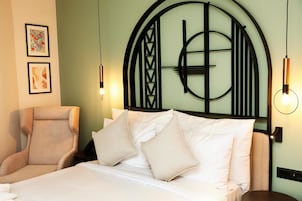 A hotel room with a bed, a chair, and a wall-mounted artwork.