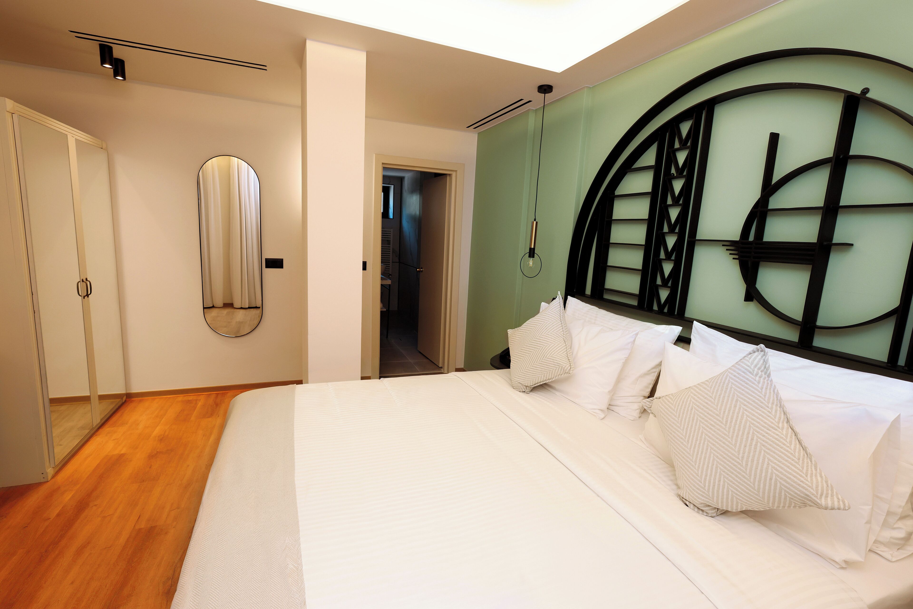 A modern bedroom with a large bed, a mirror, and a unique headboard design.
