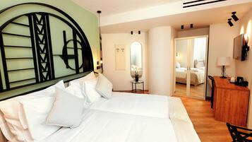 A hotel room with a large bed, a wooden desk, a mirror, and a small table with a lamp.
