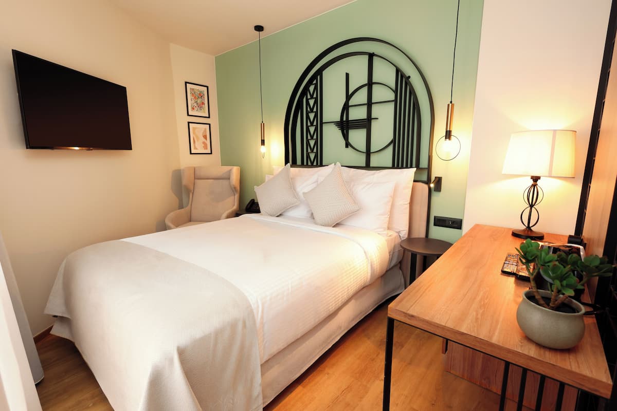Un dormitorio ordenado con cama, mesita de noche, lámpara y televisor montado en la pared.