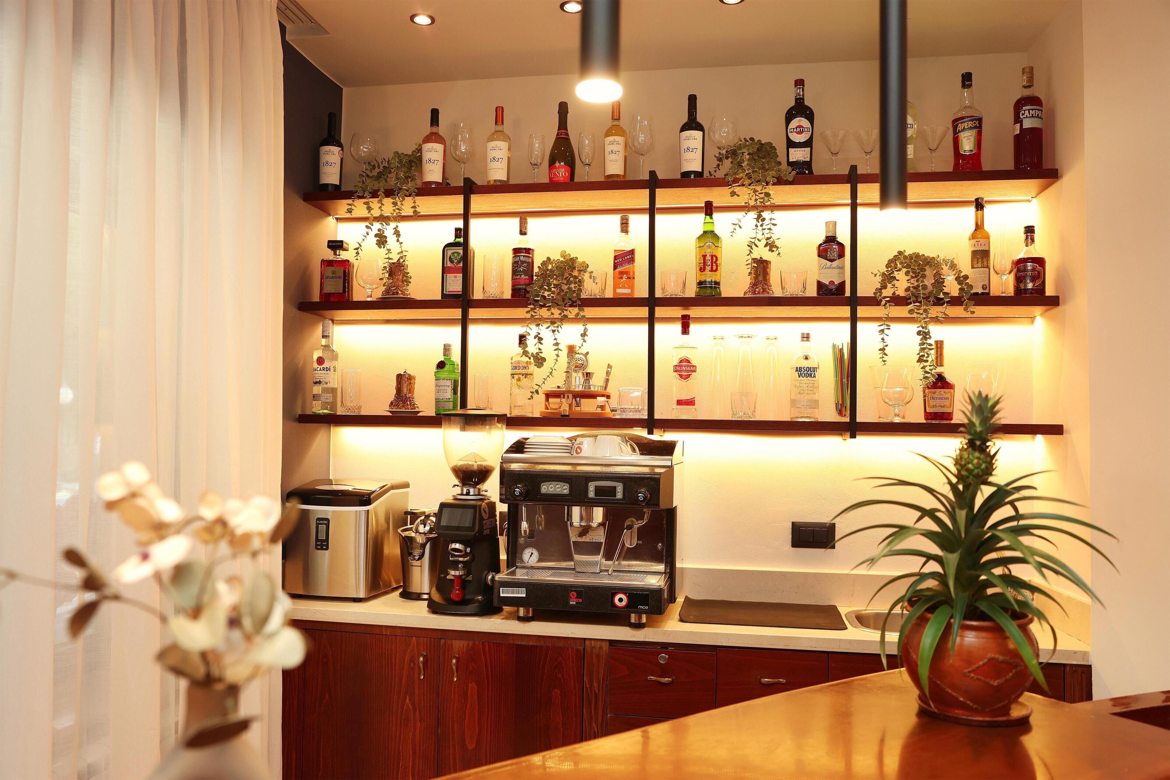 A bar area with shelves of liquor bottles and glasses, a coffee machine, and a potted plant.