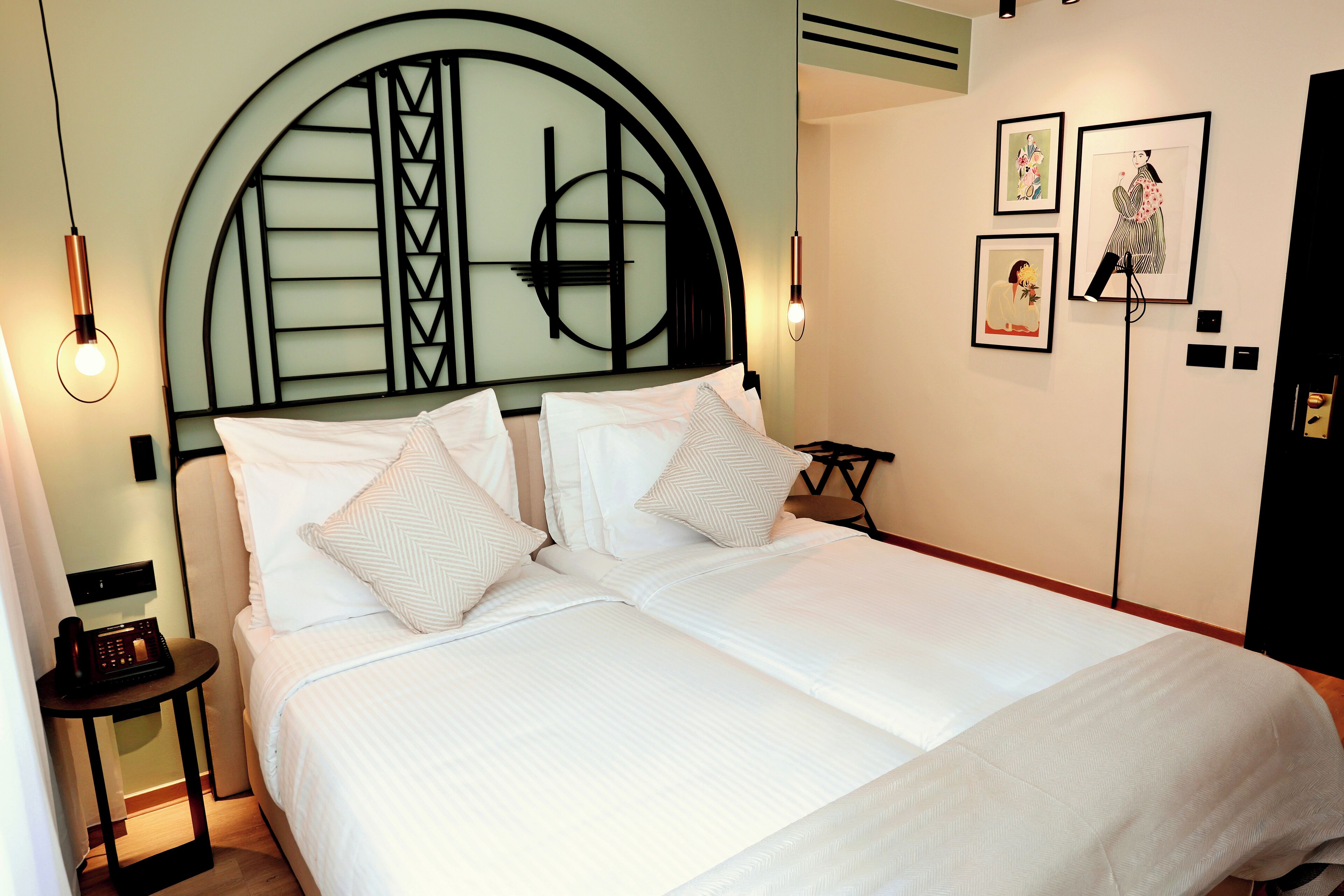 Una cama doble bien hecha con una moderna cabecera, una mesita de noche con un teléfono y una obra de arte en la pared.