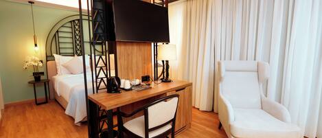 Habitación de hotel con cama, escritorio con silla, televisión y un amplio ventanal con cortinas.