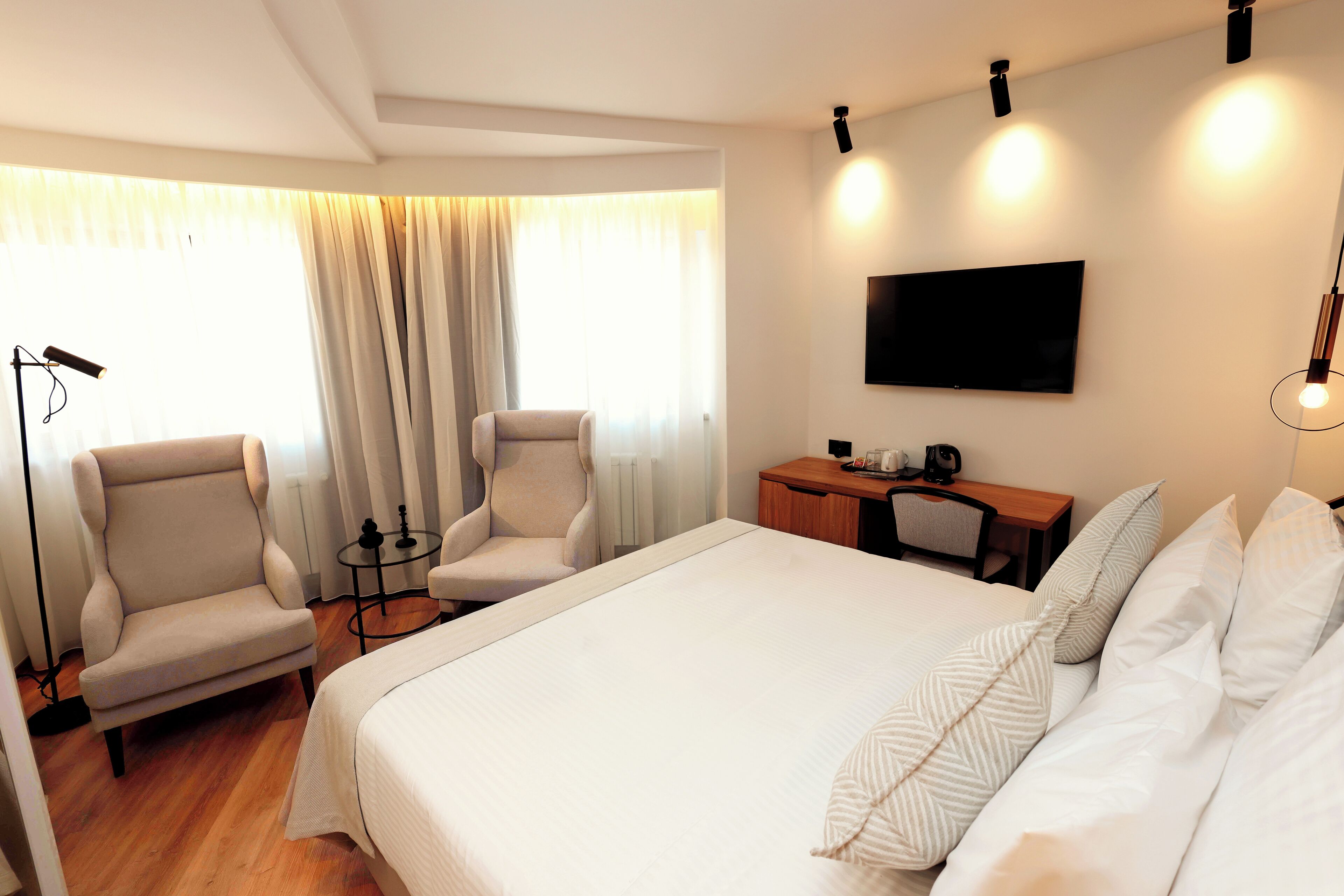 Una habitación de hotel con una cama grande, dos sillones, un escritorio y un televisor en la pared.