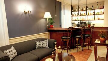 Una sala de estar moderna con un sofá gris oscuro, una mesa de centro de madera y una zona de bar con taburetes y varias botellas.