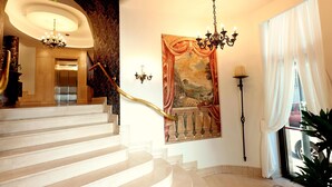 A grand staircase leading to an elevator, a chandelier, a large tapestry, and a view of the outside through a window. - Zeus Essence Bucharest Opera (Bucharest)
