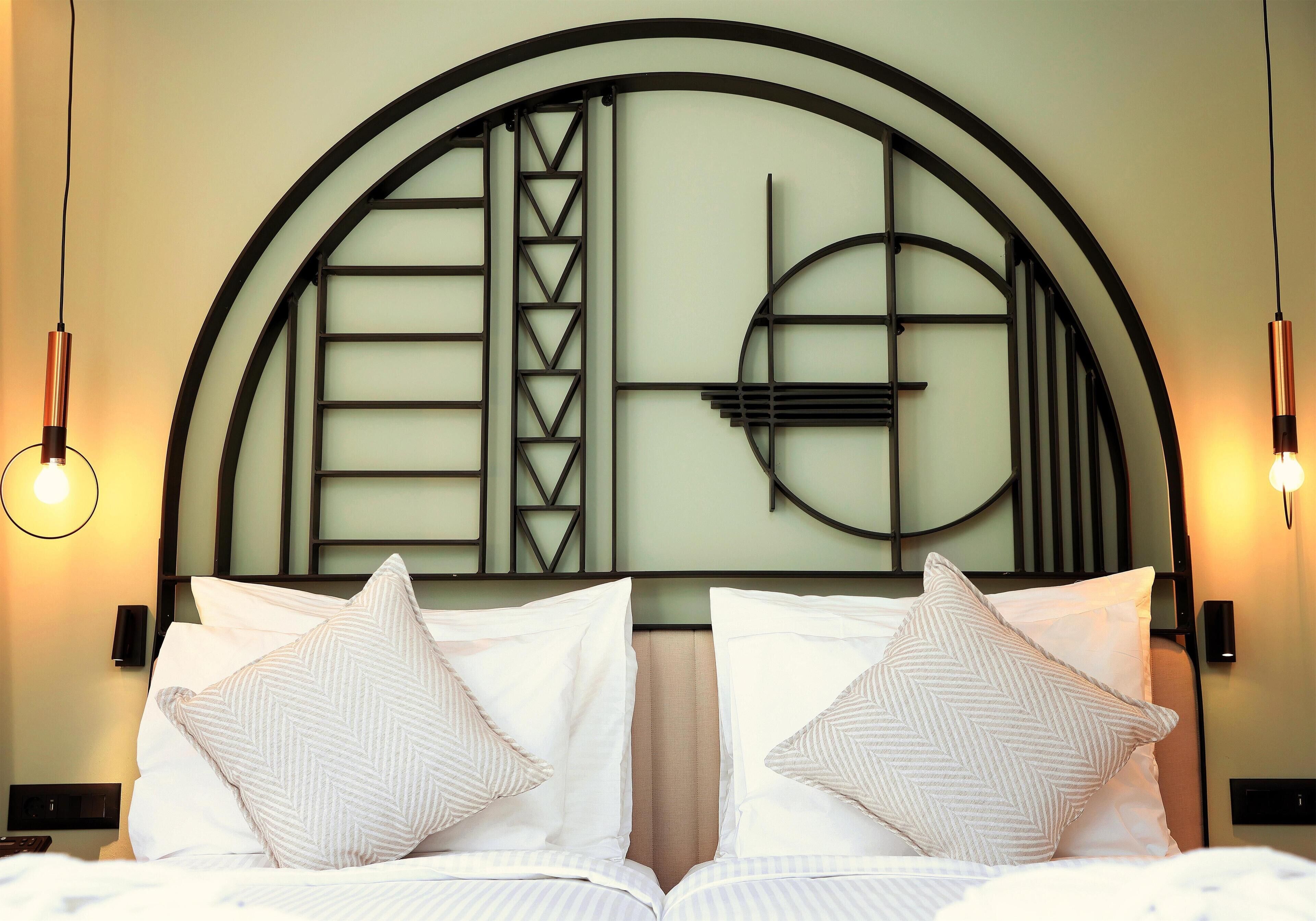 A hotel room with a large bed, two bedside lamps, and a decorative headboard with geometric patterns.
