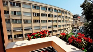 A multi-story building with a curved facade, balconies with red flowers, and a clear view of the street below. - Zeus Essence Bucharest Opera (Bucharest)