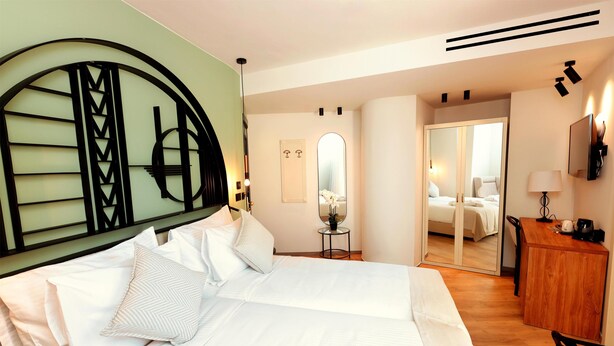 A hotel room with a large bed, a wooden desk, a mirror, and a small table with a vase. - Zeus Essence Bucharest Opera (Bucharest)