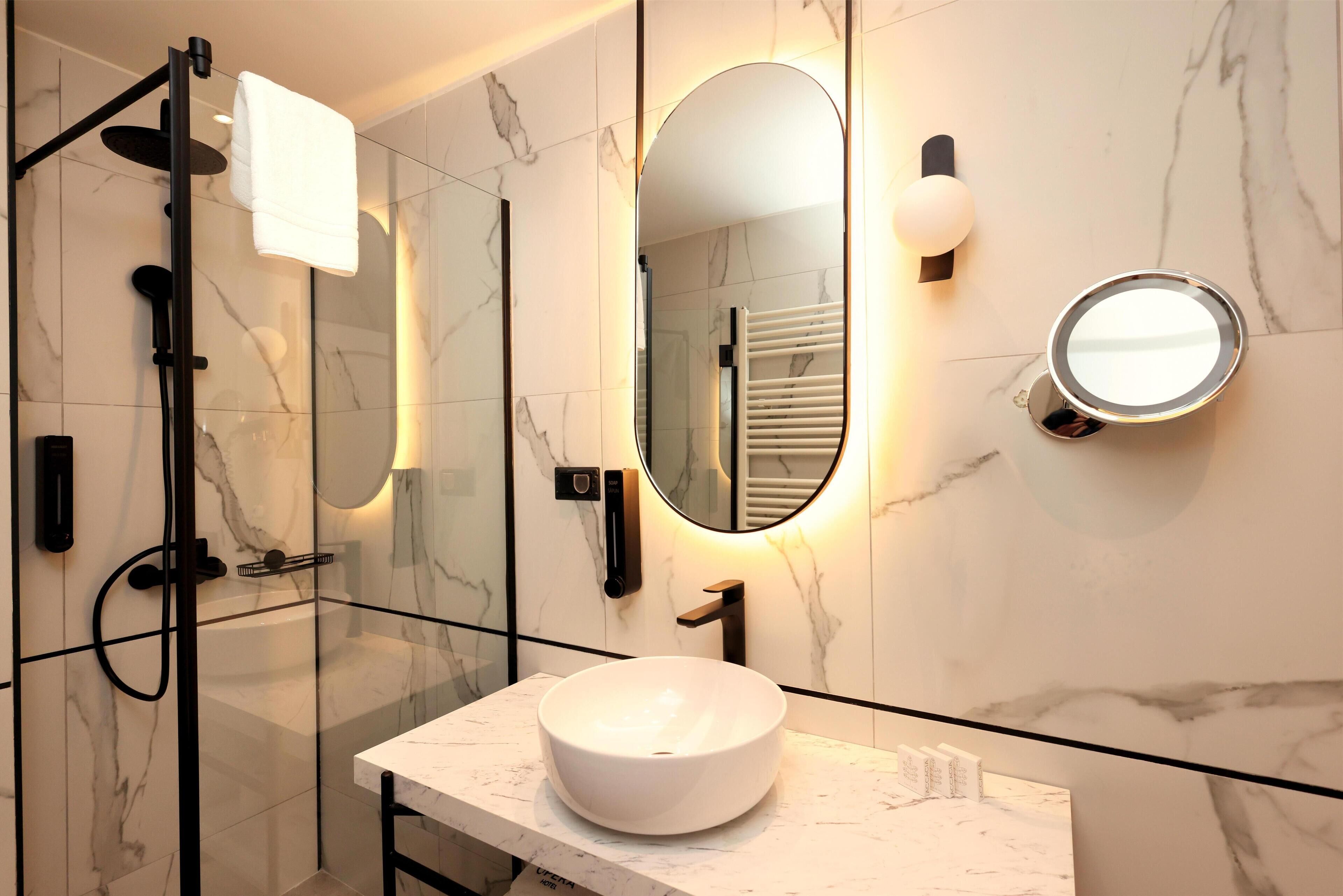 Un baño moderno con ducha de vidrio, lavamanos de mármol blanco y un espejo grande con iluminación integrada.