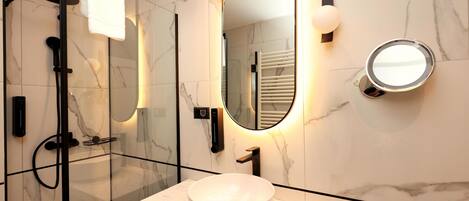 Un baño moderno con ducha de vidrio, lavamanos de mármol blanco y un espejo grande con iluminación integrada.