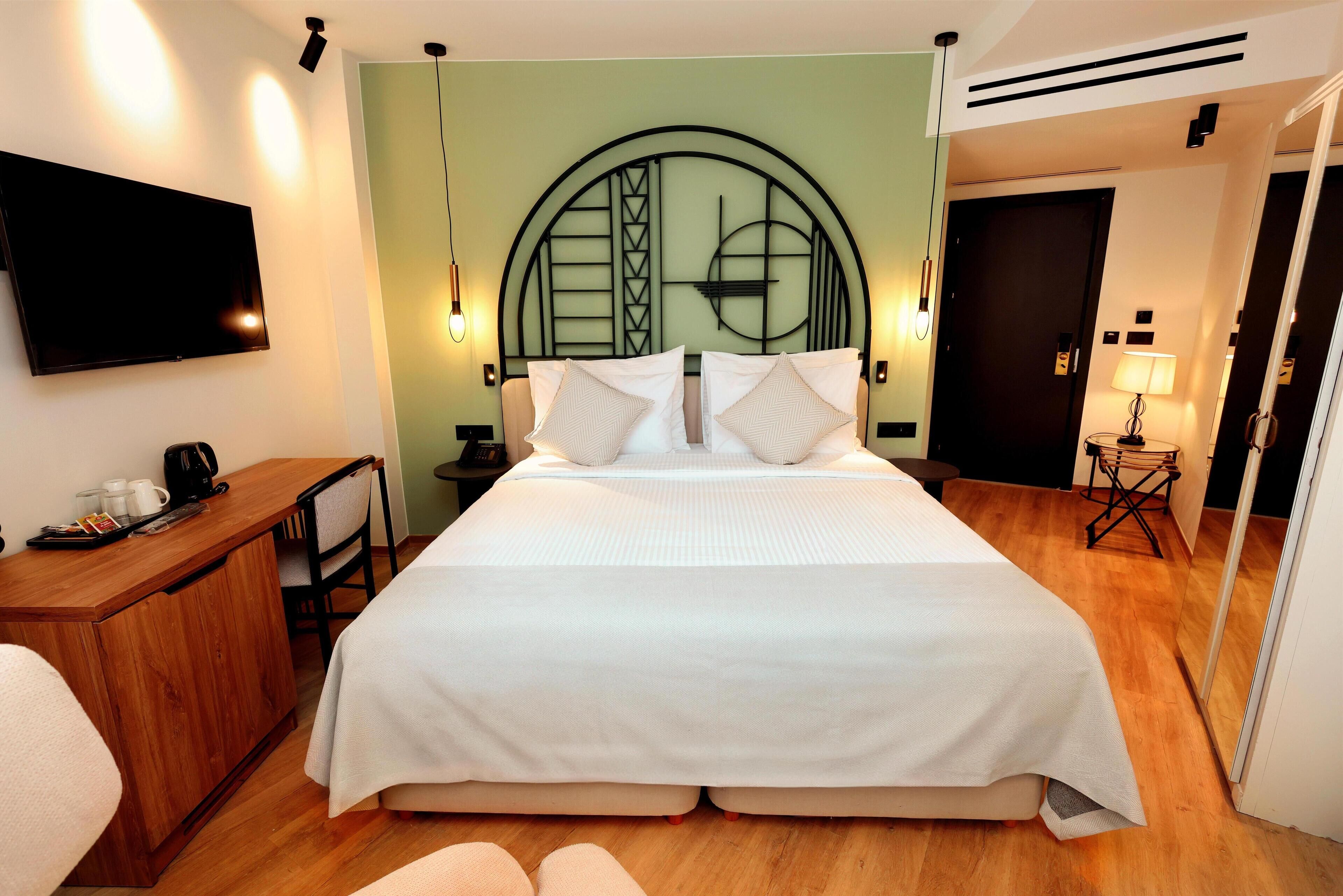 Habitación de hotel impecable con una cama grande, un escritorio con cafetera, un televisor de pantalla plana y un espejo.