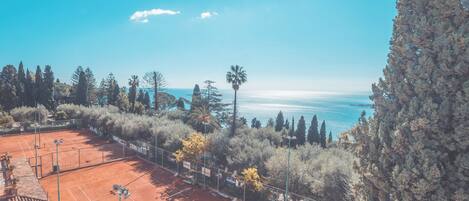 Cancha de tenis rodeada de árboles y con vista despejada al mar.