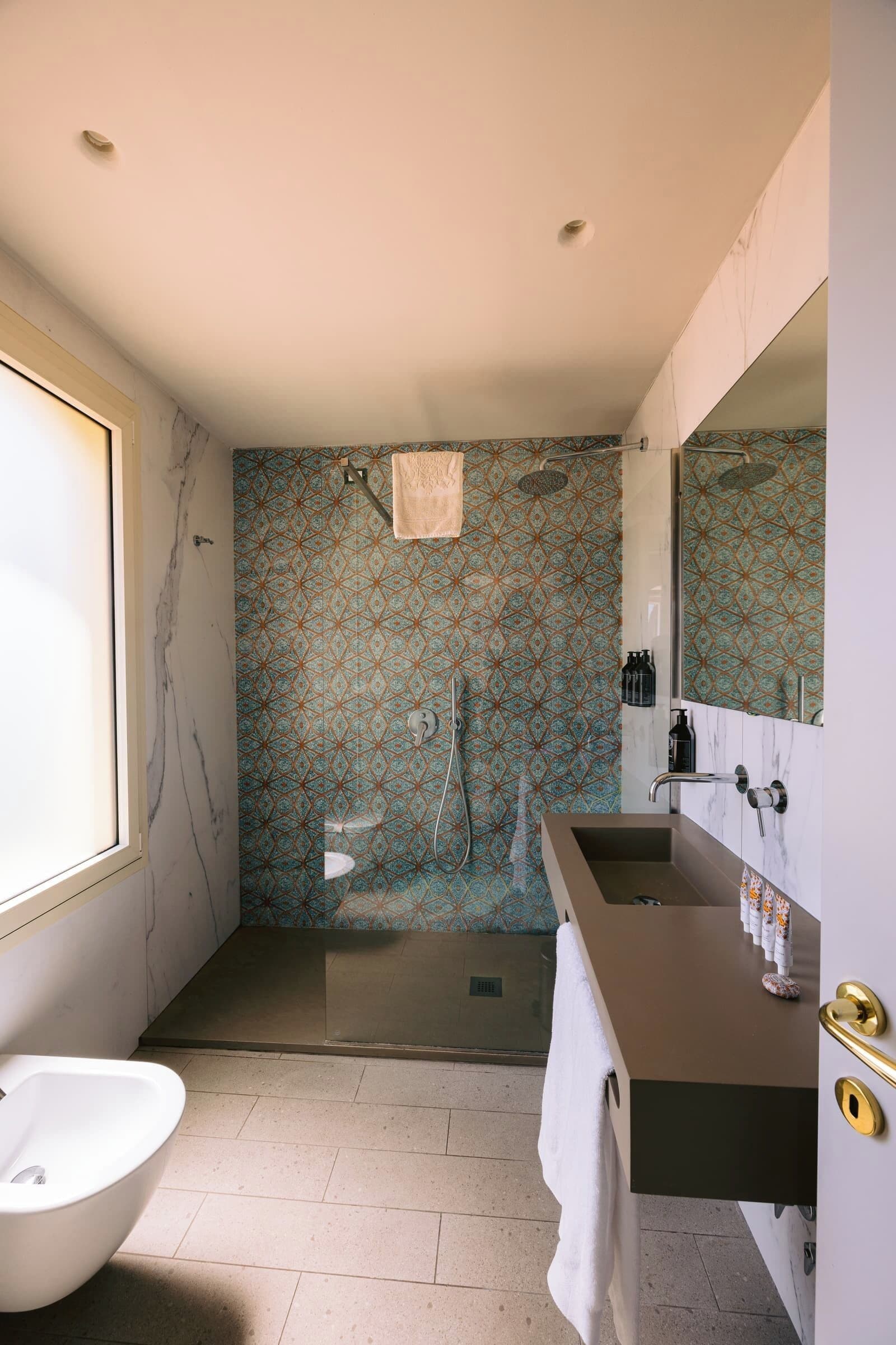 A modern bathroom with a bathtub, a shower with a patterned wall, and a vanity with a large mirror.