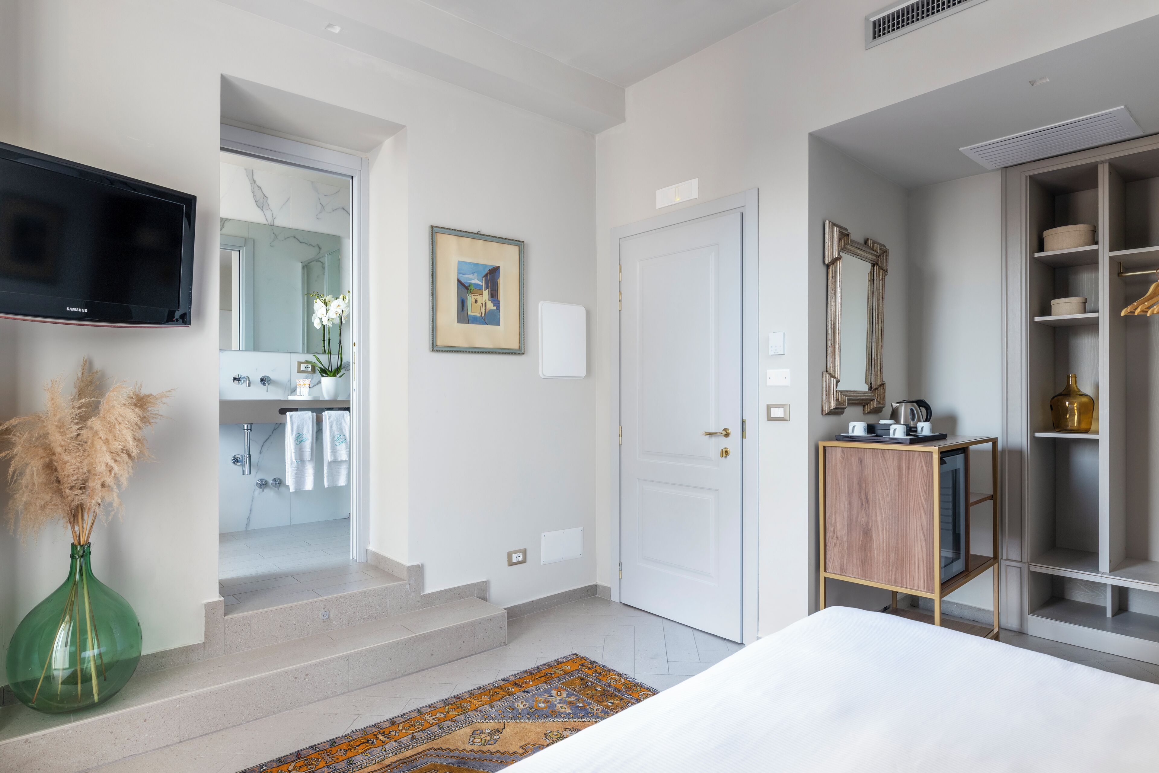 Ett hotellrum med en säng, en tv, ett badrum med en spegel, en tavla och en garderob.