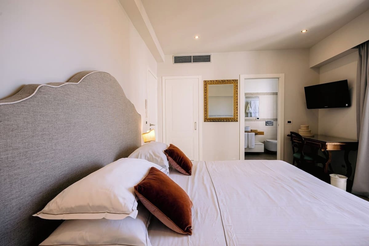 A hotel room with a large bed, a desk, a television, and a bathroom visible through an open door.