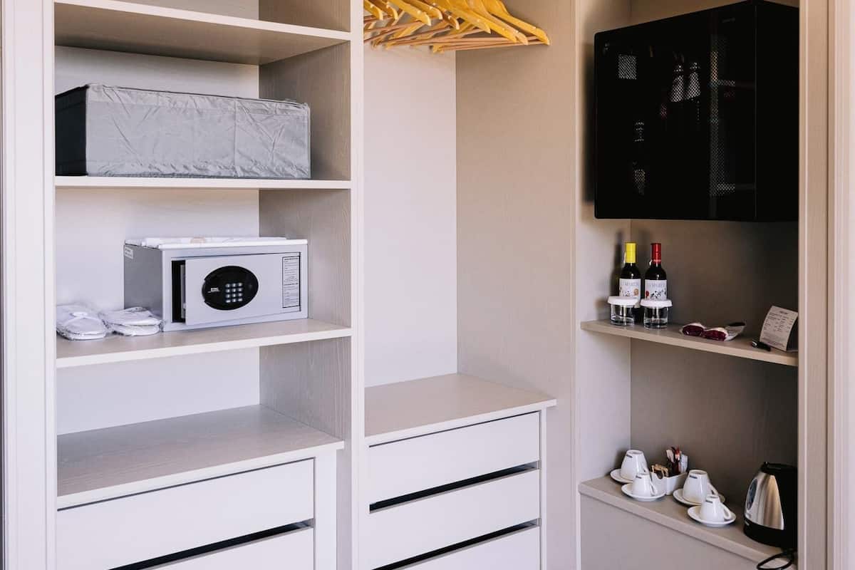 A white storage unit with shelves, a microwave, and a wine bottle.