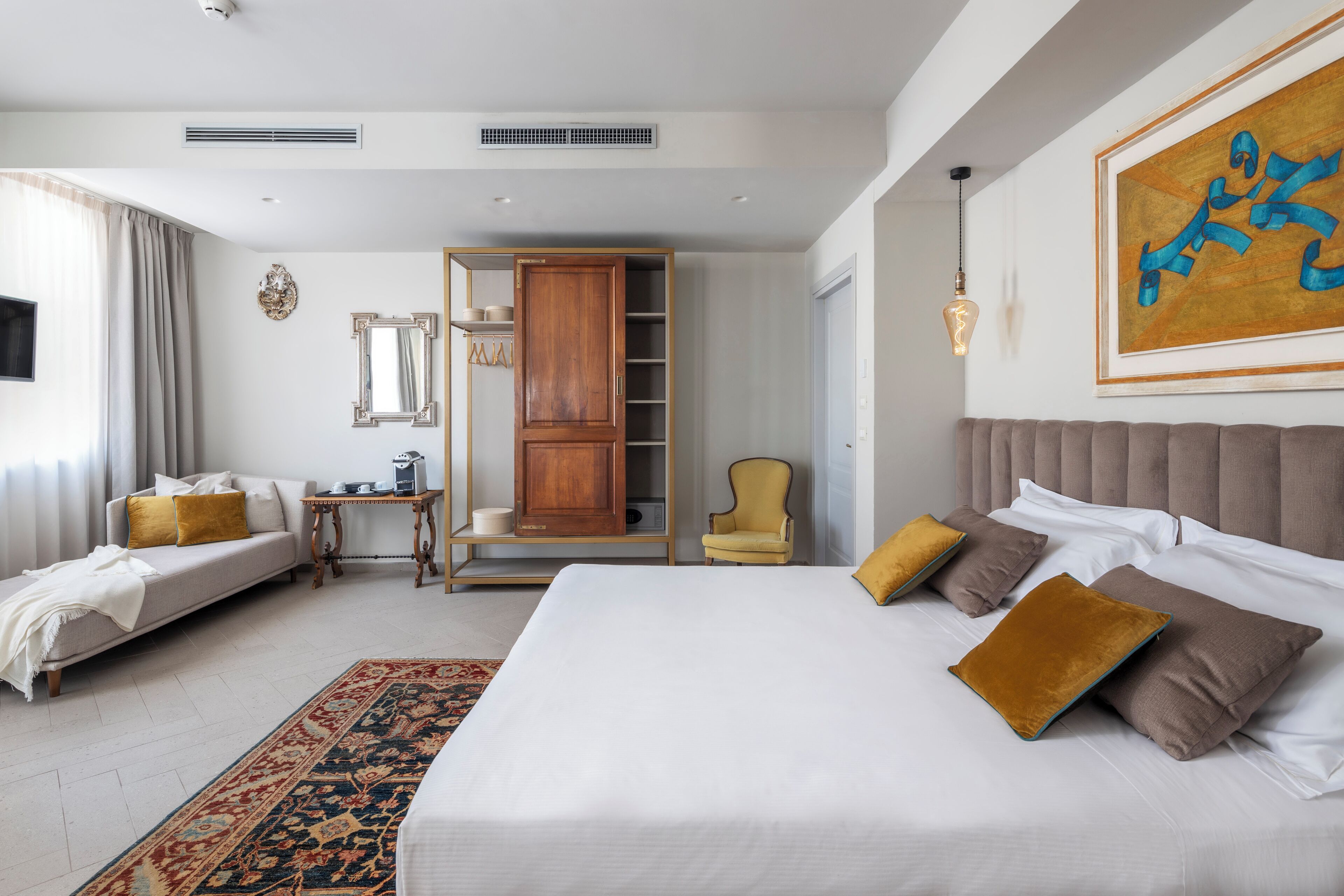 Une chambre d’hôtel avec un grand lit, un canapé, un fauteuil, une armoire et un tableau au mur.