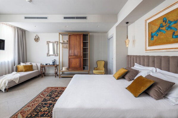 Habitación de hotel con una cama grande, un sofá, una silla, un armario y un cuadro en la pared.