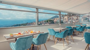 A restaurant with a view of a coastal city, featuring a terrace with tables and chairs. - Hotel Villa Paradiso (Taormina)