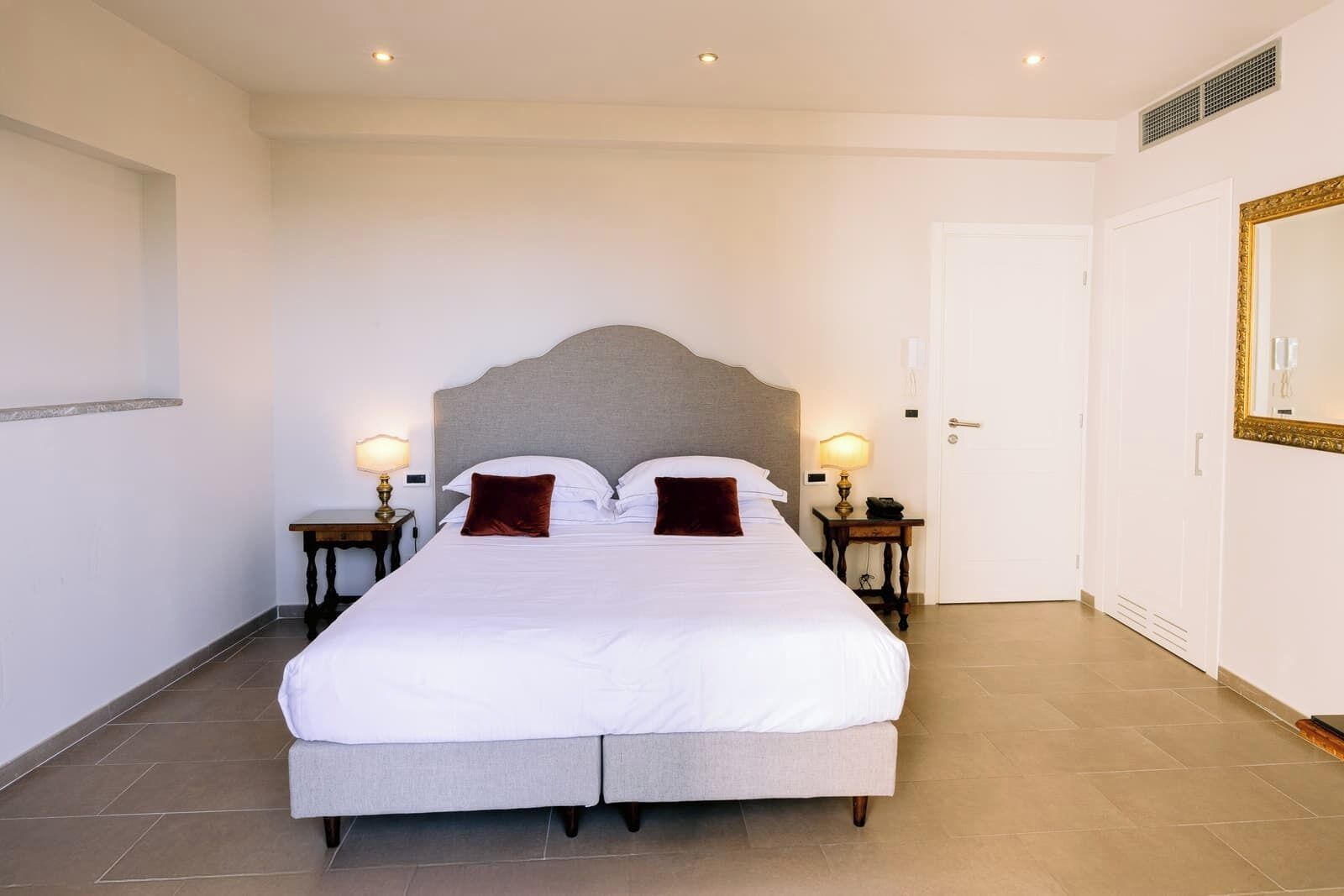 A neatly arranged bedroom with a large bed, two bedside tables with lamps, a wardrobe, and a mirror on the wall.
