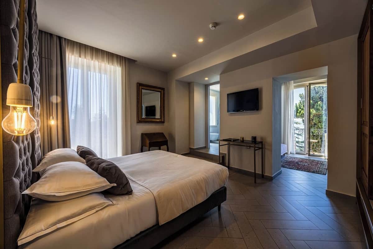 A modern hotel room with a large bed, a desk, a flat-screen TV, and a balcony with a view.