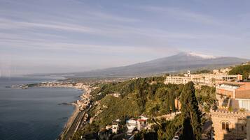 A coastal town with a prominent mountain in the background, a mix of residential and historical buildings, and a clear view of the sea.