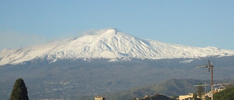 A snow-capped mountain in the background with a town in the foreground featuring buildings with arched windows and a church tower.