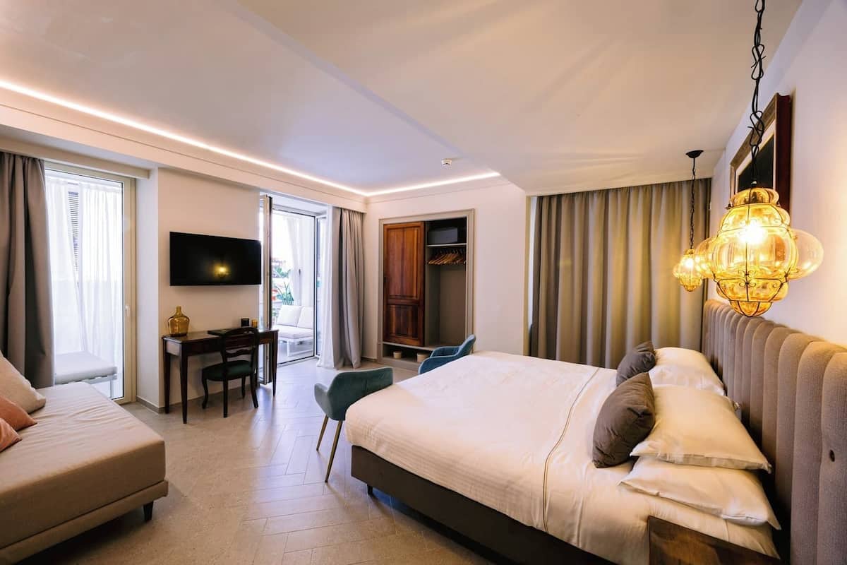 A modern hotel room with a large bed, a desk, a TV, and a balcony.