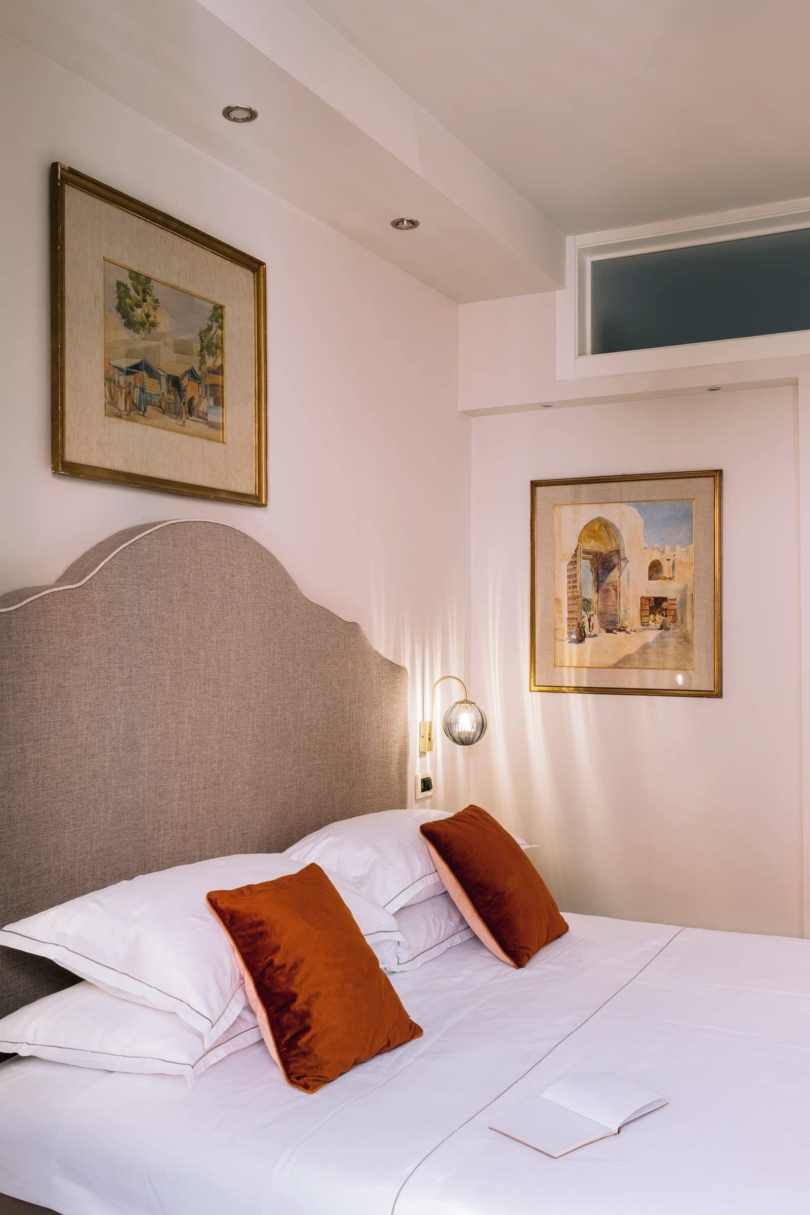 A neatly made bed with white and brown pillows, a headboard, and two framed artworks on the wall.
