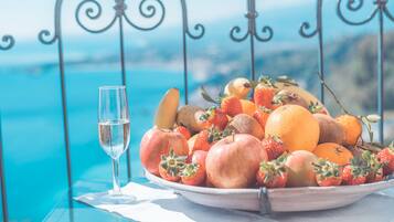 A table with a fruit bowl and a glass of water, set against a scenic view.