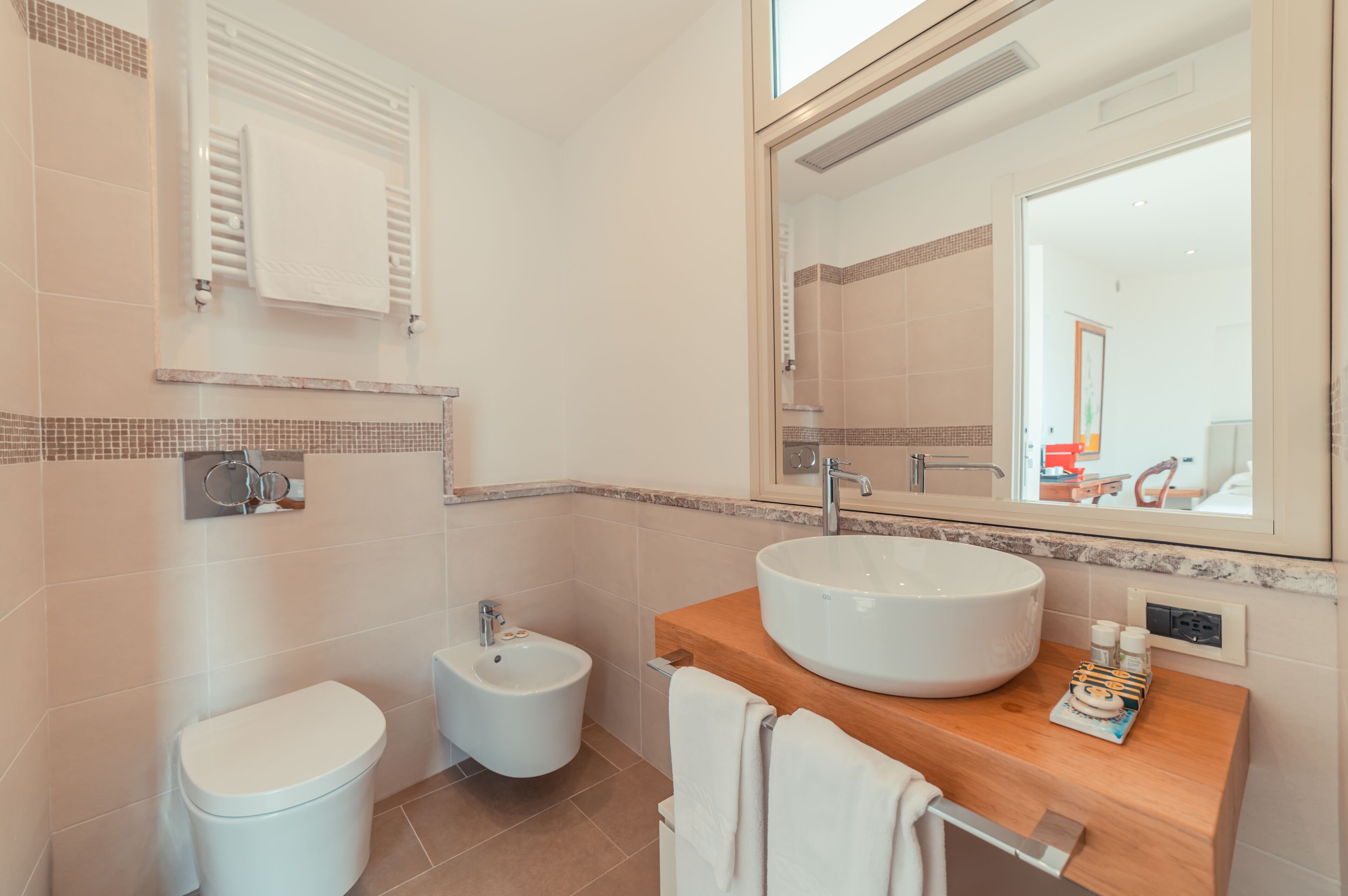 A modern bathroom with a large mirror, a round sink, a bidet, and a toilet.