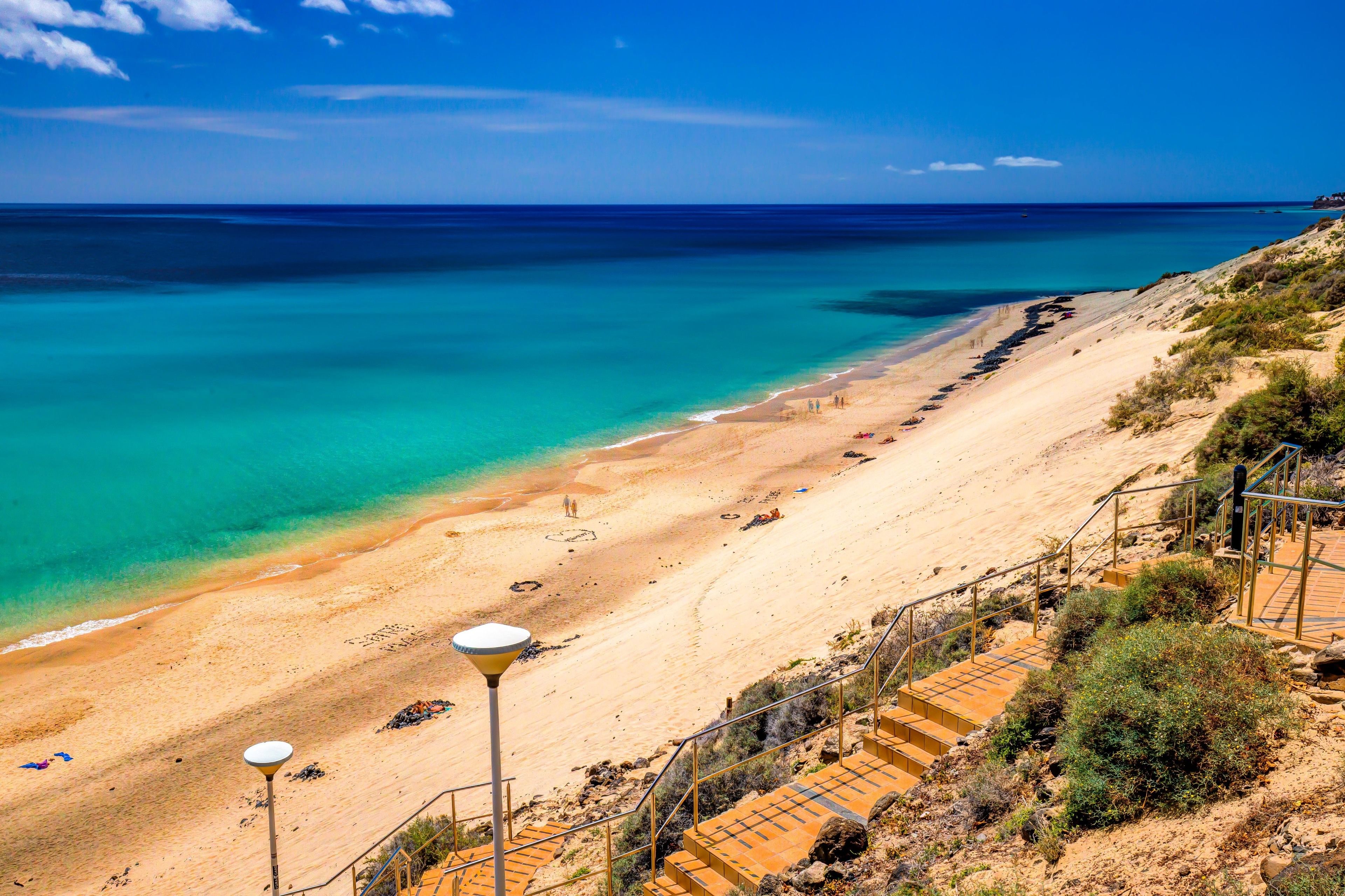 A beach with clear turquoise waters, sandy shore, and a staircase leading down to the beach.