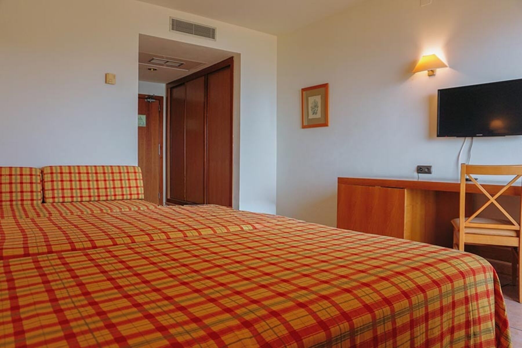 Una habitación de hotel con una cama, un escritorio, una silla, un televisor y una puerta.