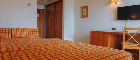 Una habitación de hotel con una cama, un escritorio, una silla, un televisor y una puerta.