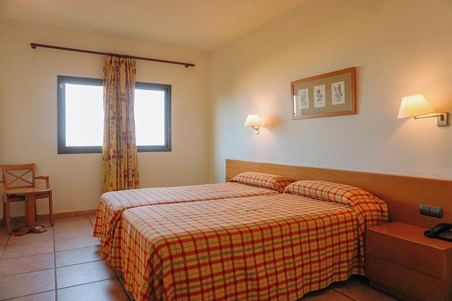 A hotel room with two beds, a chair, a nightstand, and a window with curtains.