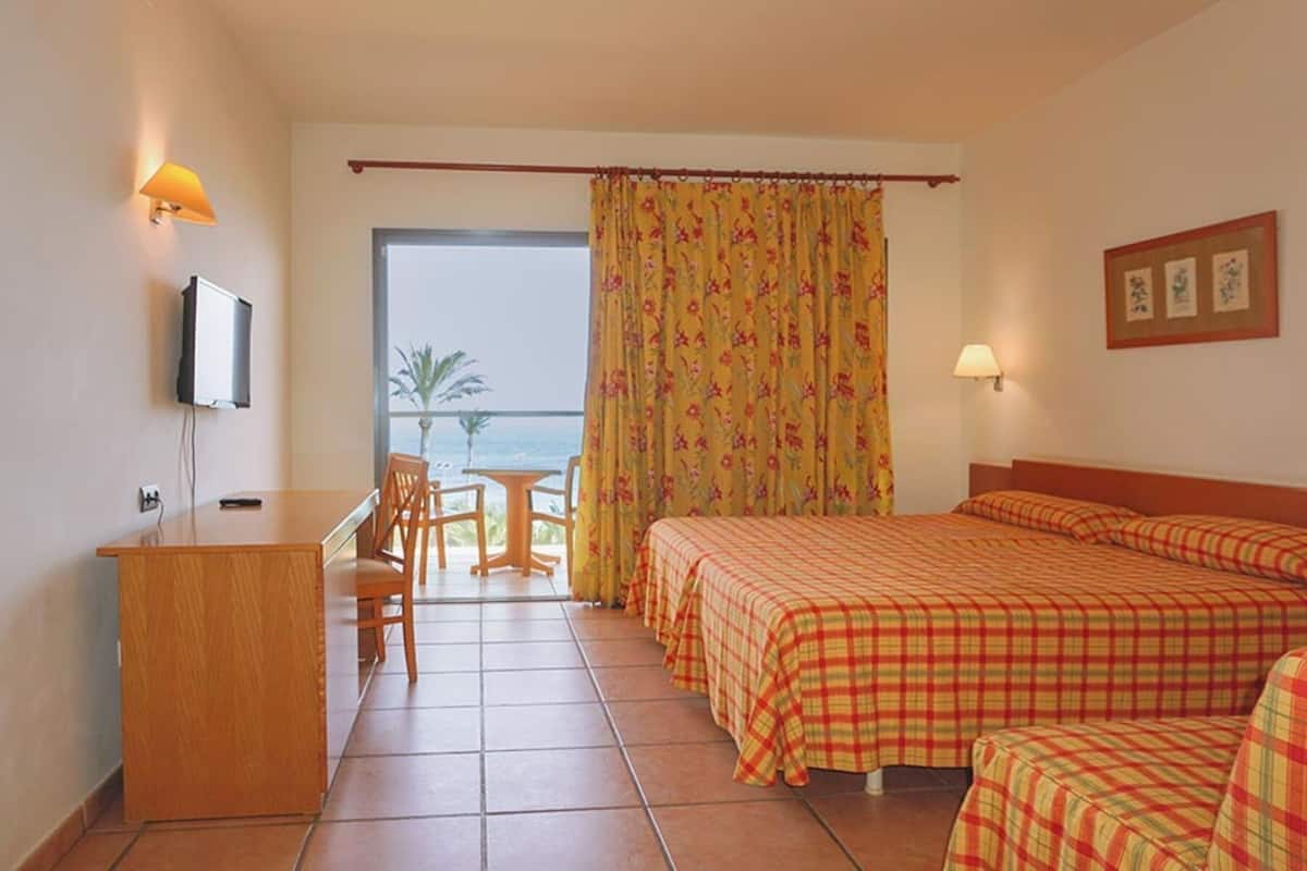 A hotel room with a bed, a desk, a chair, a TV, a window with a view, and a curtain.